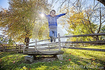 Smiling five year old boy jumping with red cape outside Stock Photo