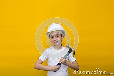 Smiling happy little girl in a construction white helmet holding a blue hammer on a yellow background Stock Photo