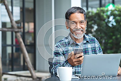 Smiling happy mature asian man with white stylish short beard using smartphone gadget serving internet at coffee shop cafe outdoor Stock Photo