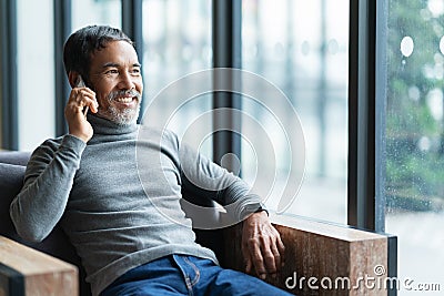 Smiling happy mature asian man with white stylish short beard using smartphone tablet talking at coffee shop cafe Stock Photo