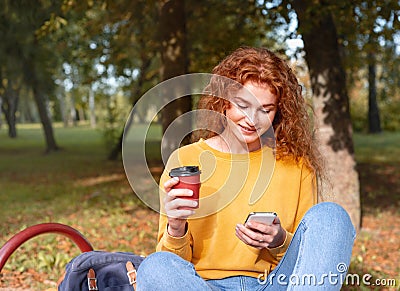 Smiling happy red hair student girl having a break with coffee outside in autumn park Stock Photo