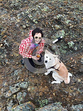 Smiling happy young girl with enameled mug with tea in hands and smart beautiful dog Japanese akita inu on a stony shore. Stock Photo