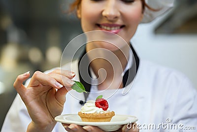 Smiling head chef putting mint leaf on little cake on plate Stock Photo