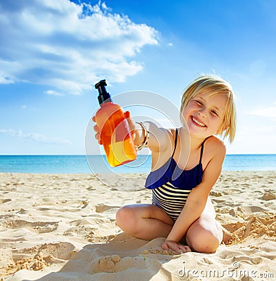 Smiling healthy child in swimwear on seacoast showing lotion Stock Photo