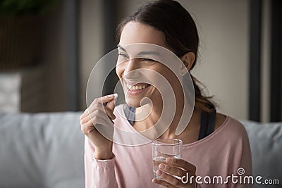 Smiling healthy woman holding pill glass of water at home Stock Photo