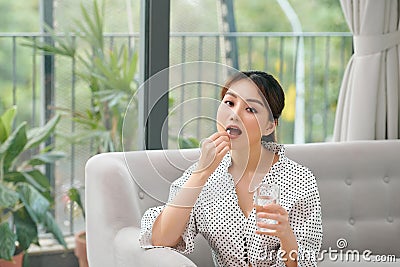 Smiling healthy young woman holding pill glass of water sit on sofa at home Stock Photo