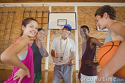 Smiling high school kids and their coach standing in the basketball court Stock Photo