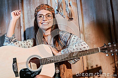 Smiling hippie girl in headband and glasses sitting with a guitar Stock Photo