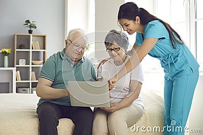 Home care nurse teaching her happy senior patients to use modern laptop computer Stock Photo