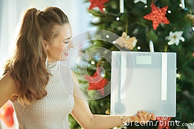 Smiling housewife near Christmas tree showing weight scales Stock Photo