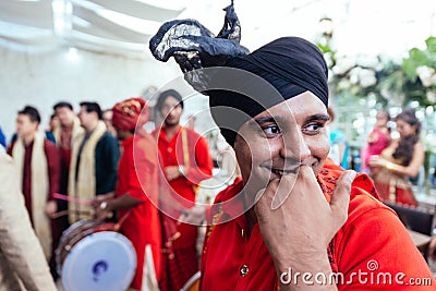 Smiling Indian musician guy wearing red Bandhgala and black Pheta at Indian wedding ceremony in Bangkok, Thailand Editorial Stock Photo