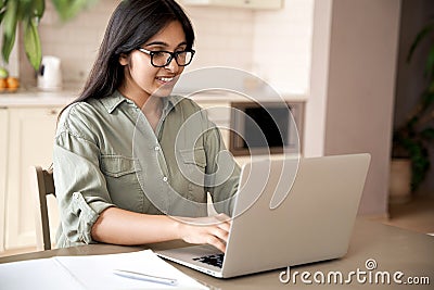 Smiling indian young woman typing on laptop computer working at home office. Stock Photo