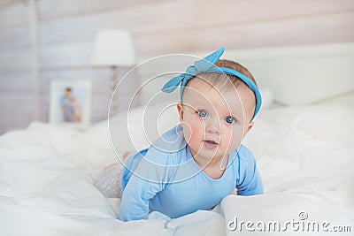 Smiling infant in blue clothes crawls on a bed in bedroom Stock Photo