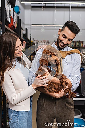Smiling interracial couple holding poodle in Stock Photo