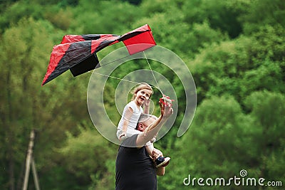 Smiling kid. Running with red kite. Child sitting on the man`s shoulders. Having fun Stock Photo