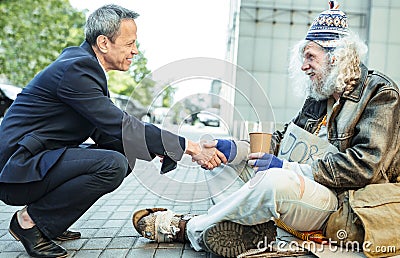 Smiling kind businessman shaking hand of starving man Stock Photo