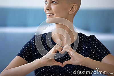 Smiling lady diagnosed with cancer holding fingers joined in heart Stock Photo