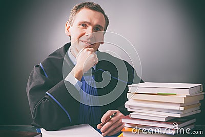 Smiling lawyer in a gown sits at a desk full of books Stock Photo