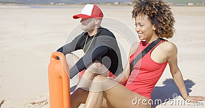 Smiling lifeguards sitting on beach Stock Photo
