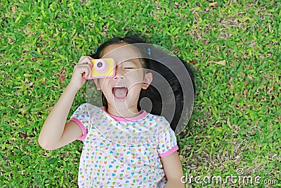 Smiling little Asian child girl with digital camera lying on green lawn background Stock Photo