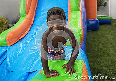 Smiling little boy sliding down an inflatable bounce house Stock Photo