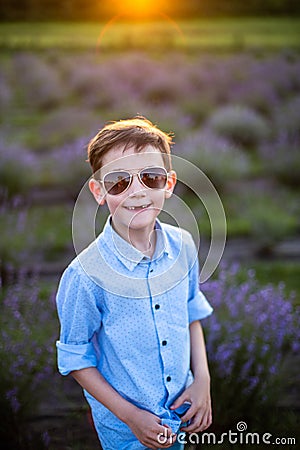 Smiling little boy standing on the lavender field. Funny child in sunglasses dressed in a blue shirt and a straw hat standing betw Stock Photo