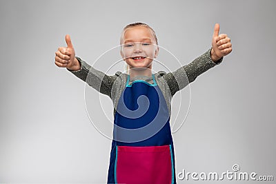 smiling little girl in apron showing thumbs up Stock Photo