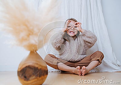 Little girl sitting in butterfly yoga position, grimasing, making finger goggles Stock Photo