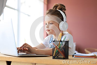 Smiling little girl in headphones handwrite study online using laptop at home Stock Photo