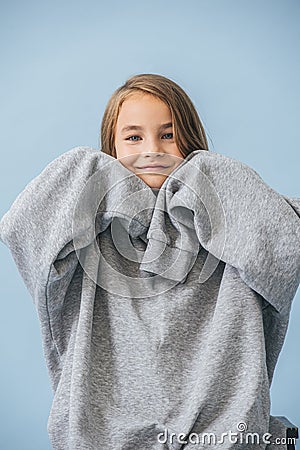 Cute smiling little girl in a huge oversized grey longsleeve over blue Stock Photo