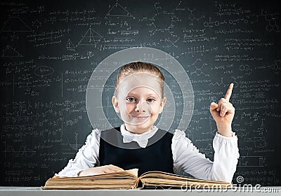 Smiling little girl sitting at desk with open book Stock Photo