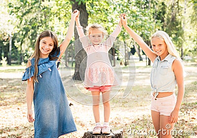 Smiling little girls stand with joyfully raised hands in park Stock Photo