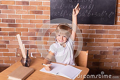 Smiling little student girl sitting at a school desk and studying math. Child pulls his hand up. Preschool education Stock Photo