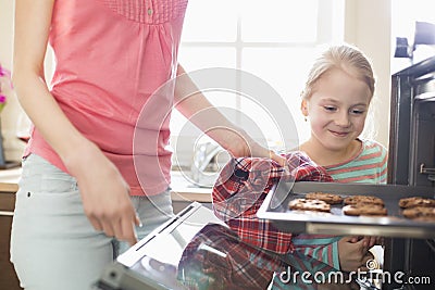 Smiling looking at mother removing cookie tray from oven at home Stock Photo