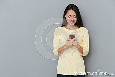 Smiling lovely young woman standing and using cell phone Stock Photo