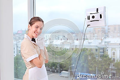 A smiling maid remotely controls a robot window cleaner. Room service. Cleaning in the hotel or in the house. Copy of the space Stock Photo