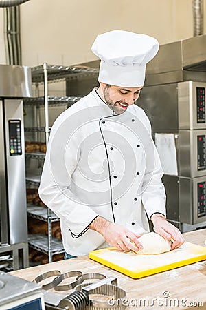 smiling male baker mashing uncooked dough Stock Photo