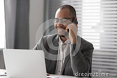 Smiling male employee working on laptop talking on cell Stock Photo