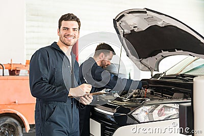 Technician Preparing Checklist While Colleague Inspecting Car In Stock Photo