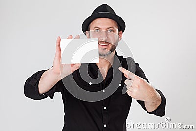 Smiling man in black shirt and black hat holding and pointing blank card Stock Photo