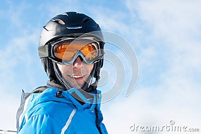 Smiling man in the blue skiing jacket, helmet and glasses against cloudy sky Stock Photo