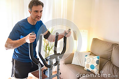 Man doing elliptical bike at home listening to music detail Stock Photo