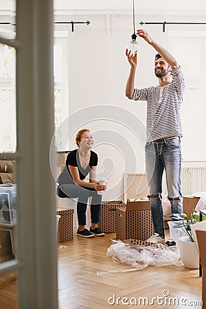 Smiling man hanging lamp while furnishing new home after moving in with his happy wife Stock Photo