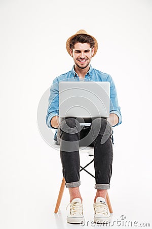 Smiling man in hat sitting on chair and using laptop Stock Photo