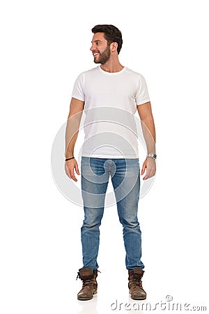 Smiling Man In Jeans And White T-shirt Is Standing And Looking Away. Front View Stock Photo