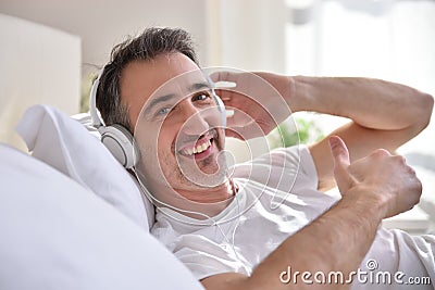 Smiling man listening music lying in bed ok sign Stock Photo