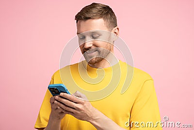 Smiling man looking at smartphone screen, browsing in internet chatting with friends over pink wall Stock Photo