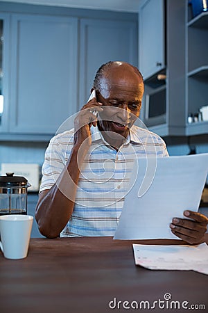 Smiling man reading document while using phone at home Stock Photo