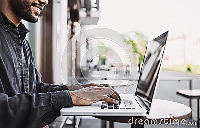 Smiling man using laptop computer in a city. Young handsome student having coffee break. Stock Photo