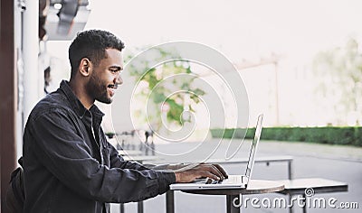 Smiling man using laptop computer in a city. Young handsome student having coffee break. Stock Photo